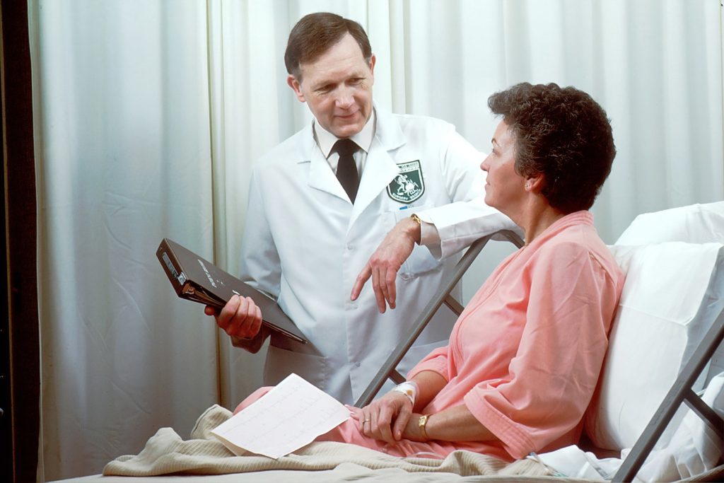 Male doctor standing beside a female patient in bed